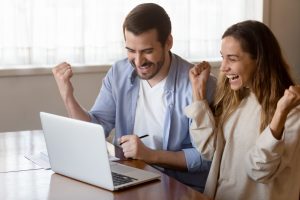 Overjoyed young couple celebrating success, looking at laptop screen
